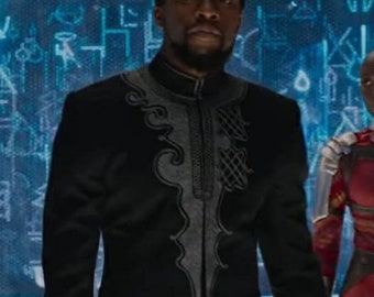 May include: A man wearing a black suit jacket with silver embroidery. The jacket has a high collar and a decorative design on the front. The man is standing in front of a blue background with white symbols.