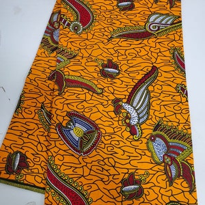 May include: Orange fabric with a paisley pattern in black, red, white, and yellow. The fabric has the text "GUARANTEED WAX" printed on it.