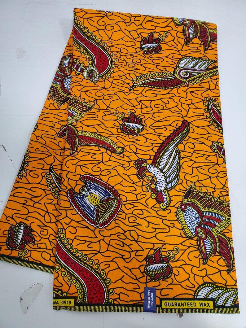May include: Orange fabric with a paisley pattern in black, red, white, and yellow. The fabric has the text "GUARANTEED WAX" printed on it.