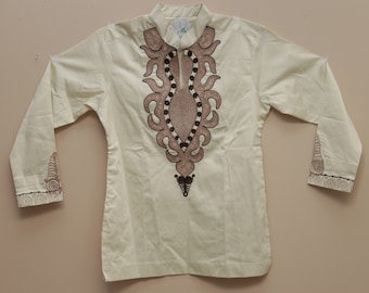 Può includere: Una camicia bianca a maniche lunghe con un ricamo marrone e beige sul davanti. Il ricamo presenta un motivo geometrico con una forma ovale centrale.