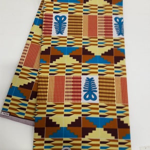 May include: A yellow, brown, blue, and red patterned fabric with a repeating geometric design. The fabric has a white label with the text "SUPREME KENTE HOLLAND" printed on it.