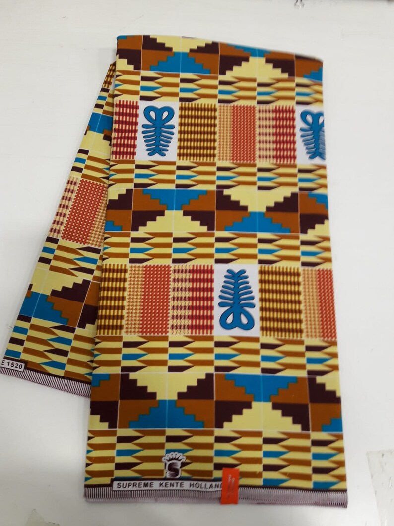 May include: A yellow, brown, blue, and red patterned fabric with a repeating geometric design. The fabric has a white label with the text "SUPREME KENTE HOLLAND" printed on it.