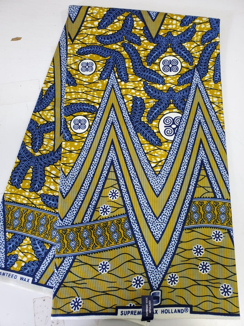 May include: A yellow and blue patterned fabric with a geometric design. The fabric has a white border with the text "SUPREME WAX HOLLAND" printed on it.