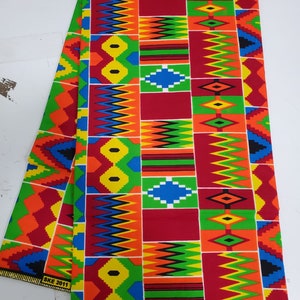 May include: A colorful fabric with a geometric pattern in shades of red, yellow, green, blue, and black. The fabric has a repeating pattern of squares and diamonds. The fabric is folded in half and the edges are visible. The fabric has the text "SKE 2011" printed on the bottom edge.