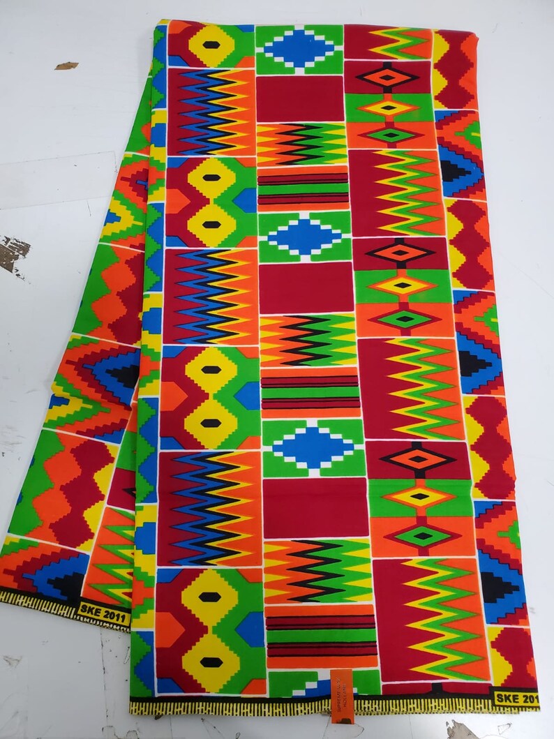 May include: A colorful fabric with a geometric pattern in shades of red, yellow, green, blue, and black. The fabric has a repeating pattern of squares and diamonds. The fabric is folded in half and the edges are visible. The fabric has the text "SKE 2011" printed on the bottom edge.