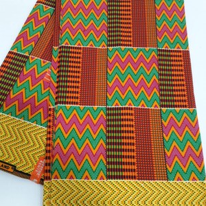 May include: A folded piece of fabric with a colorful geometric pattern in shades of orange, yellow, green, pink, and brown. The fabric has a zig-zag pattern and a checkered pattern. The fabric has the text "SUPREME KENTE HOLL" printed on it.