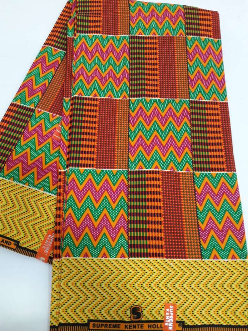 May include: A folded piece of fabric with a colorful geometric pattern in shades of orange, yellow, green, pink, and brown. The fabric has a zig-zag pattern and a checkered pattern. The fabric has the text "SUPREME KENTE HOLL" printed on it.