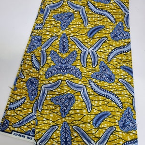 May include: A yellow and blue patterned fabric with a repeating design of stylized leaves. The fabric has the text "SUPREME WAX" and "GUARANTEED WAX" printed on the bottom edge.