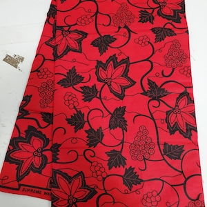 May include: Red fabric with a black floral pattern featuring grapes and leaves. The fabric has the text "SUPREME WAX GUARANTEED HOLLAND" printed on it.