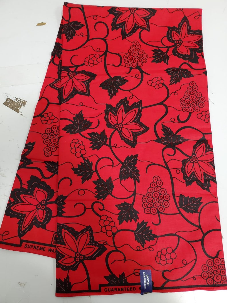 May include: Red fabric with a black floral pattern featuring grapes and leaves. The fabric has the text "SUPREME WAX GUARANTEED HOLLAND" printed on it.
