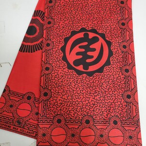 May include: Red fabric with a black and white pattern. The pattern features a large circle with a symbol inside, surrounded by smaller circles. The fabric has the text "SUPREME WAX HOLLAND" and "VERITABLE WAX HOLLAND" printed on it.