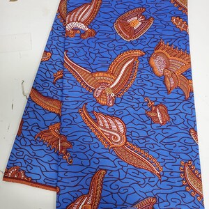 May include: Blue fabric with a repeating pattern of orange and white stylized birds and paisley shapes. The fabric has the text "SUPREME WAX HOLLAND&reg;" printed on the bottom edge.