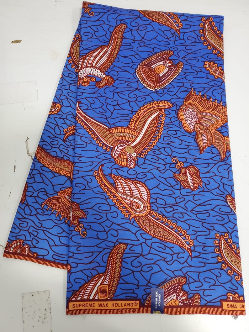 May include: Blue fabric with a repeating pattern of orange and white stylized birds and paisley shapes. The fabric has the text "SUPREME WAX HOLLAND&reg;" printed on the bottom edge.