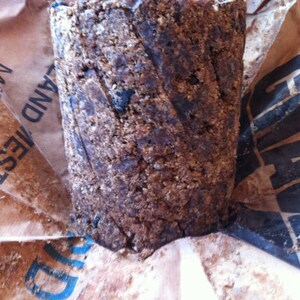 May include: A close-up of a brown, rough-textured, cylindrical block of soap wrapped in brown paper. The paper has the text "LAND AESTIVE" printed on it.