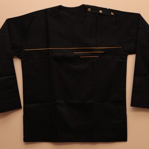May include: A black long-sleeved shirt with a gold trim design. The shirt has a round neckline and a button closure at the neck.
