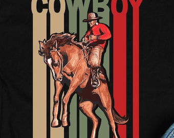 May include: Black t-shirt featuring a vintage-style graphic of a cowboy riding a bucking horse. The graphic has a red, green and yellow colour scheme and the word "COWBOY" is printed above the image.