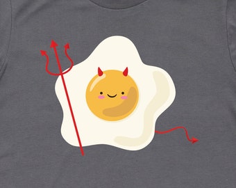 Op de afbeelding: Een antracietgrijs T-shirt met een afbeelding van een cartoon-ei met duivelshoorns en een hooivork. Het ei glimlacht en heeft een geel eigeel.