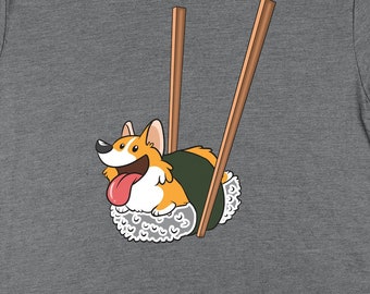 May include: A gray t-shirt with a cartoon image of a corgi dog dressed as a sushi roll. The corgi is being held up by two chopsticks.