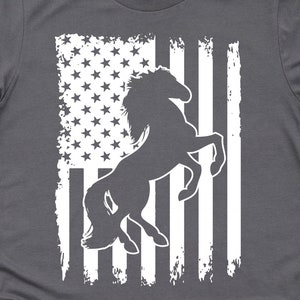 May include: A charcoal grey t-shirt with a white silhouette of a horse rearing up in front of a distressed American flag design.