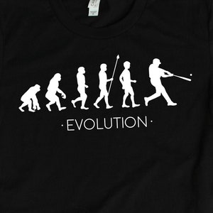 Op de afbeelding: Zwart T-shirt met een witte afbeelding van de evolutie van de mens, eindigend met een honkballer. De tekst "EVOLUTION." is onder de afbeelding gedrukt.