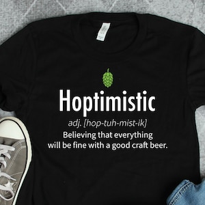 Può includere: Maglietta nera con un design grafico bianco che dice "Hoptimistic" e definisce la parola come "Credere che tutto andrà bene con una buona birra artigianale."