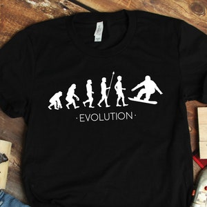 May include: Black t-shirt with a white graphic of the evolution of man, ending with a stick figure snowboarding. The text "EVOLUTION." is below the graphic.