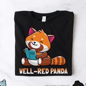 May include: Black t-shirt featuring a cartoon red panda reading a book. The panda is orange, brown, and white, with pink accents. The text "WELL-RED PANDA" is below the panda. The shirt also has the text "MULTIPLE STYLES AVAILABLE!"