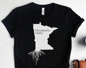 Op de afbeelding: Zwart T-shirt met een witte omtrek van de staat Minnesota en de tekst "Minnesota Roots" met witte boomwortels die zich uitstrekken vanaf de onderkant van de staat.