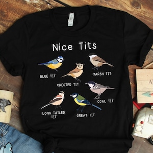 May include: A black t-shirt with a humorous design featuring different types of birds with the text "Nice Tits" and the names of each bird type below them: Blue Tit, Crested Tit, Marsh Tit, Coal Tit, Long Tailed Tit, and Great Tit.