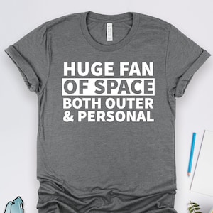 以下が含まれることがあります： グレーのTシャツに、白い文字で「Huge Fan of Space Both Outer & Personal」と書いてあります。