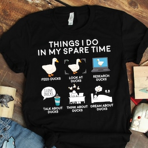 May include: Black t-shirt with white text that reads "Things I do in my spare time". The shirt features a list of activities related to ducks, including feeding, looking at, researching, talking about, thinking about, and dreaming about ducks.