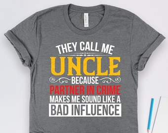 Könnte beinhalten: Graues T-Shirt mit dem Text "They call me Uncle because partner in crime makes me sound like a bad influence" in gelber und roter Schrift.
