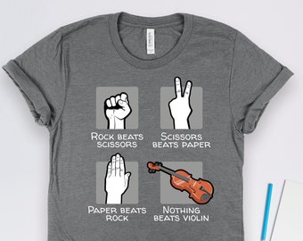 May include: A grey t-shirt featuring a graphic of the classic game "Rock, Paper, Scissors" with a twist. The graphic depicts the traditional hand gestures for rock, paper, and scissors, but the fourth option is a violin with the text "Nothing Beats Violin".