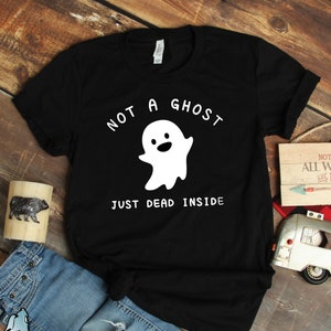 Puede incluir: Camiseta negra con un gr&aacute;fico de un fantasma blanco y el texto "No es un fantasma, solo muerto por dentro".