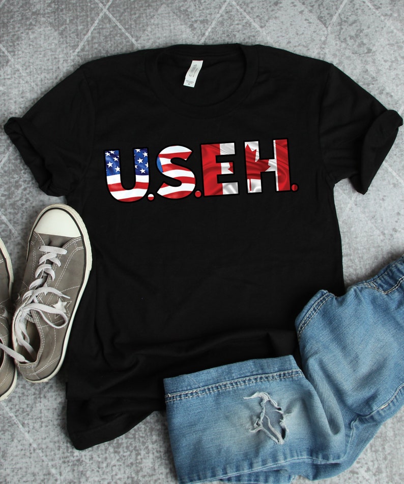 May include: Black t-shirt with the word "U.S.E.H." written in large letters. The letters are made up of the American and Canadian flags.