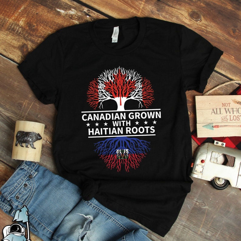Puede incluir: Camiseta negra con un dise&ntilde;o de &aacute;rbol con las banderas de Canad&aacute; y Hait&iacute;. El texto dice "Canadian Grown with Haitian Roots".