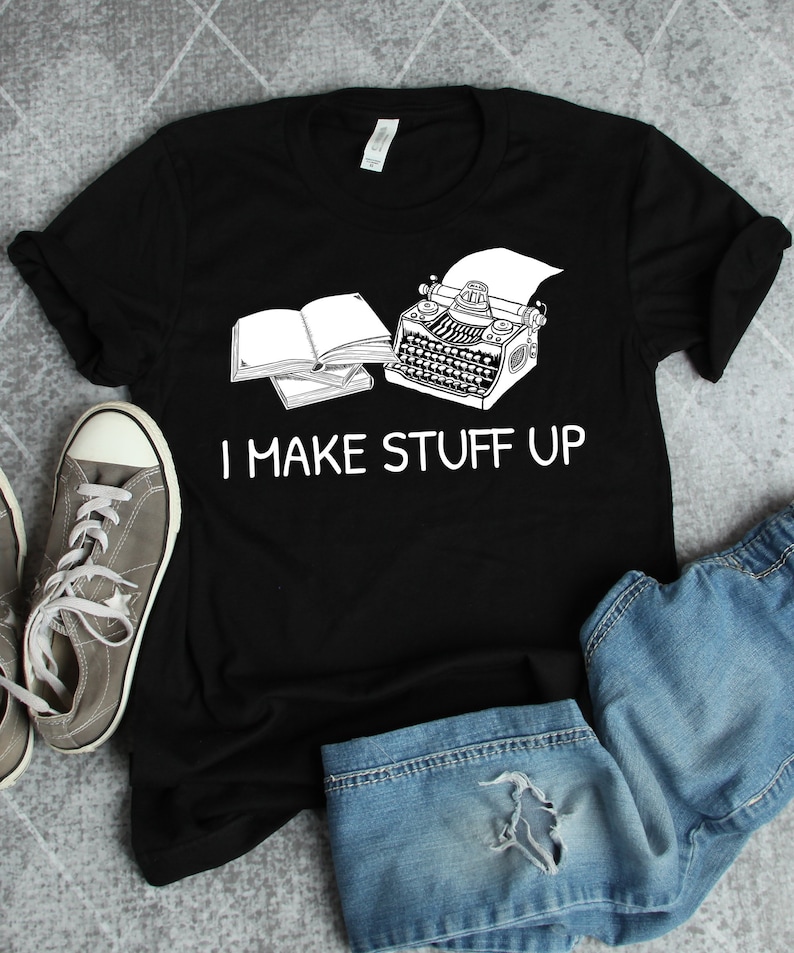 May include: Black t-shirt with a white graphic of a typewriter and a book. The text "I MAKE STUFF UP" is printed below the graphic.