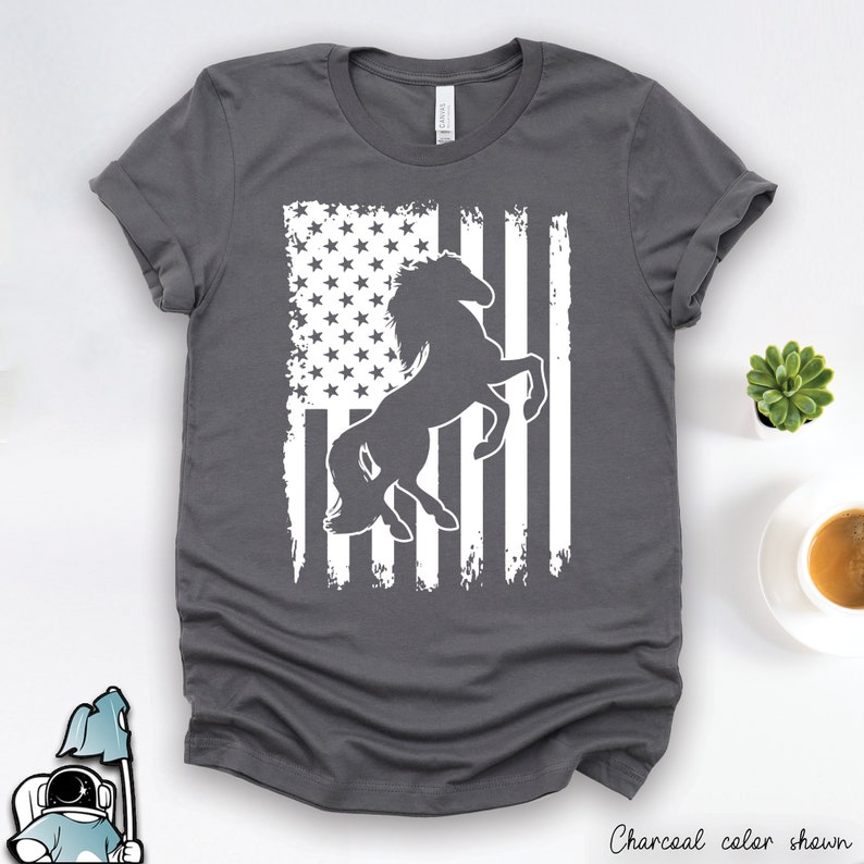 May include: A charcoal grey t-shirt with a white silhouette of a horse rearing up in front of a distressed American flag design.