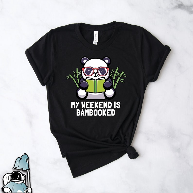 Może przedstawiać: Czarny T-shirt z kresk&oacute;wkowym pandą w czerwonych okularach czytającym książkę. Panda jest otoczony bambusem. Pod pandą znajduje się napis "My weekend is bamboooked".