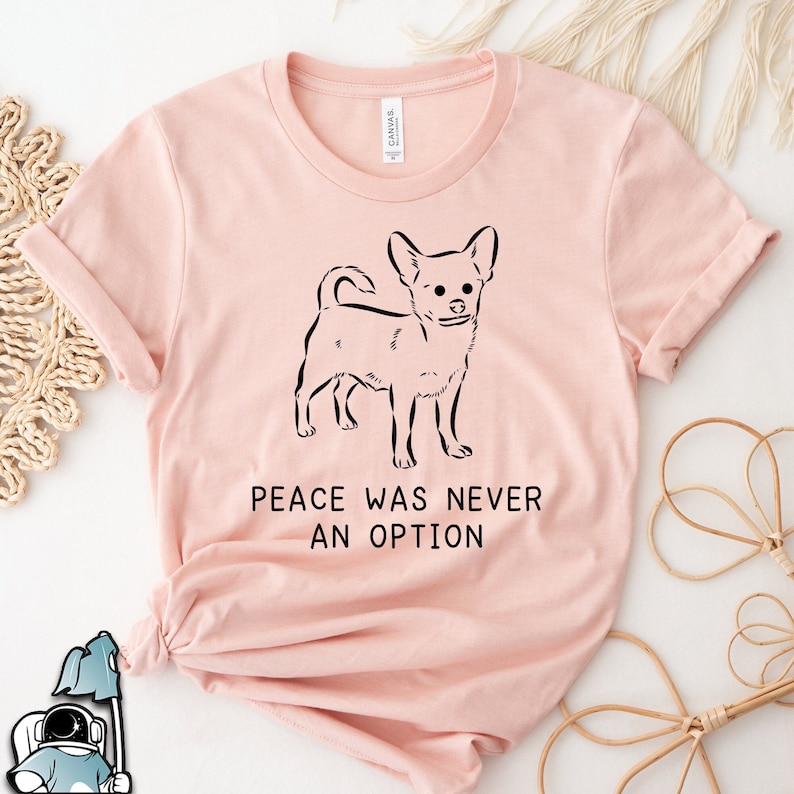 Puede incluir: Una camiseta rosa con un contorno negro de un chihuahua y el texto "Peace was never an option".