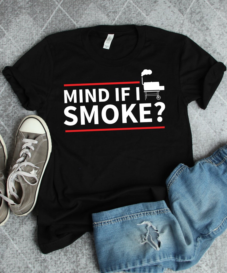 May include: Black t-shirt with the text "MIND IF I SMOKE?" in white with a red line above and below the text. A white silhouette of a grill with smoke coming out of the chimney is to the right of the text.