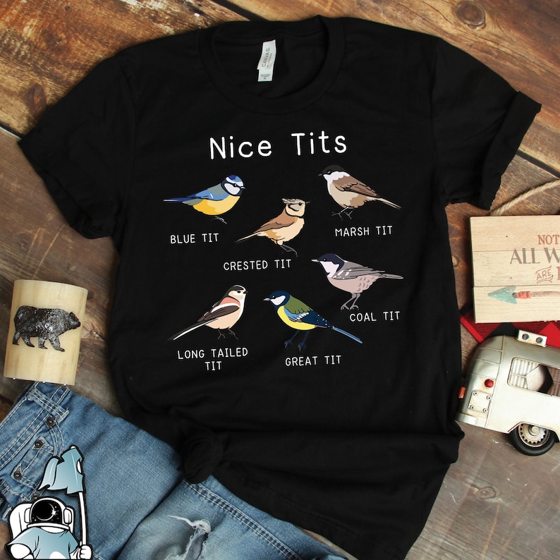 May include: A black t-shirt with a humorous design featuring different types of birds with the text "Nice Tits" and the names of each bird type below them: Blue Tit, Crested Tit, Marsh Tit, Coal Tit, Long Tailed Tit, and Great Tit.