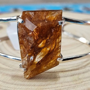 May include: A silver bangle bracelet with a large, faceted, brown and gold crystal set in the center.