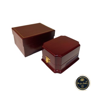 May include: Two wooden boxes, one larger than the other. The larger box is a dark red colour with a gold trim. The smaller box is a slightly lighter shade of red with a gold latch. Both boxes have a smooth, polished finish.
