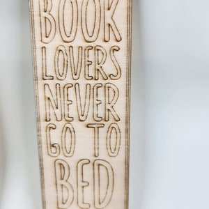 May include: A wooden bookmark with the text "BOOK LOVERS NEVER GO TO BED ALONE" engraved on it. The bookmark has a gold string attached to the top.