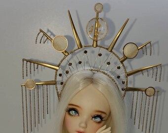 May include: A gold crown with a delicate wire design and small circular accents. The crown is adorned with dangling chains and has a pointed, starburst-like shape.