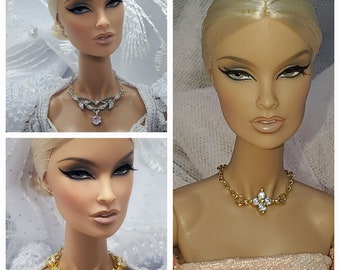 May include: A collage of three images showcasing a doll with blonde hair and dramatic eye makeup. The doll is wearing different necklaces, including a silver necklace with a pink pendant, and a gold necklace with a blue gem.