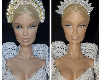 May include: Two doll portraits side-by-side, each wearing a different jeweled crown. The left doll has a gold-toned, half-circle crown with large, clear stones. The right doll wears a silver-toned, spiky crown. Both dolls have blonde hair, dramatic eye makeup, and wear white crocheted tops.