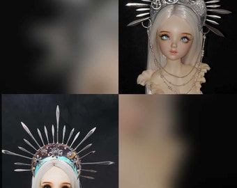 May include: A silver crown with a crescent moon design and spikes, worn by a doll with long blonde hair and blue eyes.