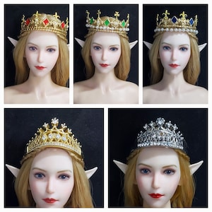 Puede incluir: Cinco coronas diferentes de oro y plata con gemas de varios colores. Las coronas están en maniquíes con cabello rubio y orejas de elfo.